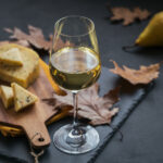 A glass of white wine served with cheese in a cutting board on d